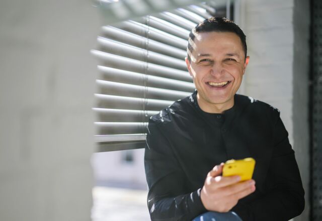 NOVIA GmbH Consulting und Baumanagement - Projektleiter sitzt am Fenster und schaut lachend von seinem Smartphone auf