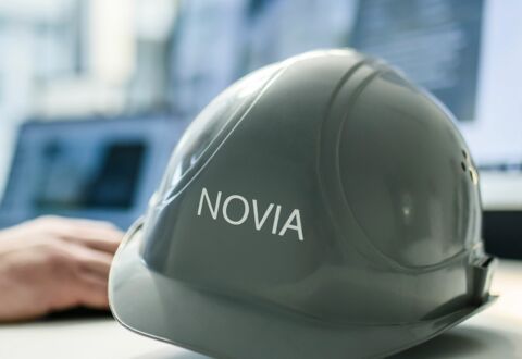 NOVIA GmbH Consulting und Baumanagement - Detailaufnahme: Baumhelm mit NOVIA-Logo liegt auf Schreibtisch eines Mitarbeiters.